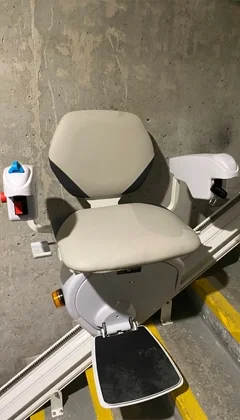 A beige stair lift chair with black footrest installed along straight staircase.