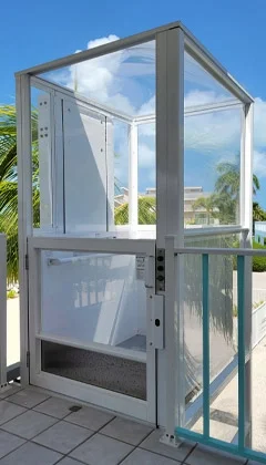 Multilift vertical platform lift with a white frame on a balcony, overlooking palm trees and a bright blue sky.