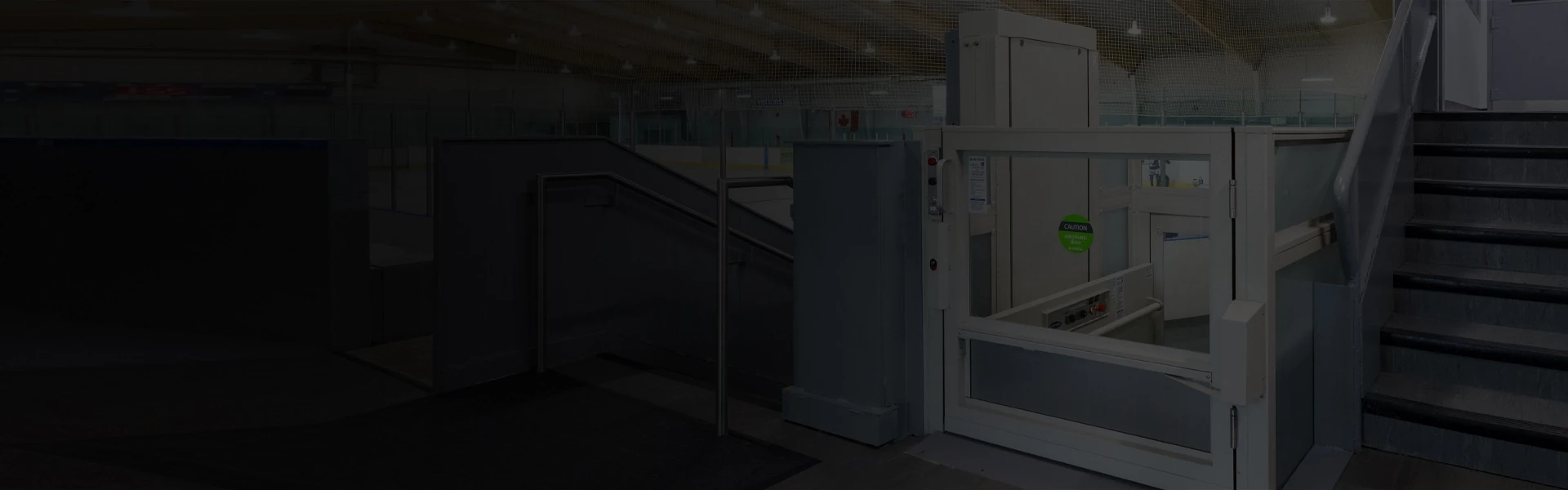 Vertical platform lift installed beside an arena stairway, featuring a gated entry and enclosed platform for accessible travel between levels.