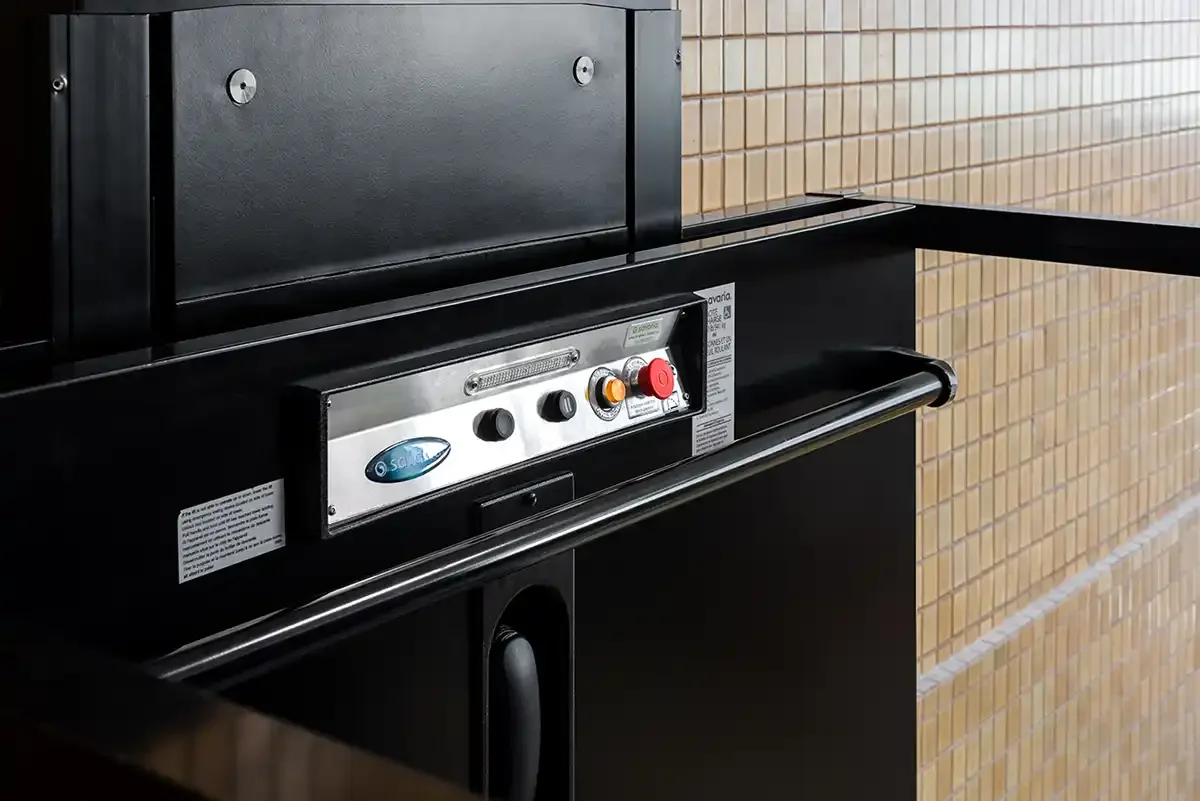 Close-up of Savaria platform lift control panel with floor buttons, emergency stop, alarm button, and stainless steel handrail
