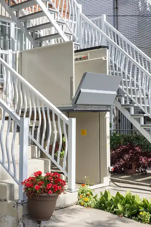 Outdoor wheelchair platform lift installed beneath exterior stairs with safety gate