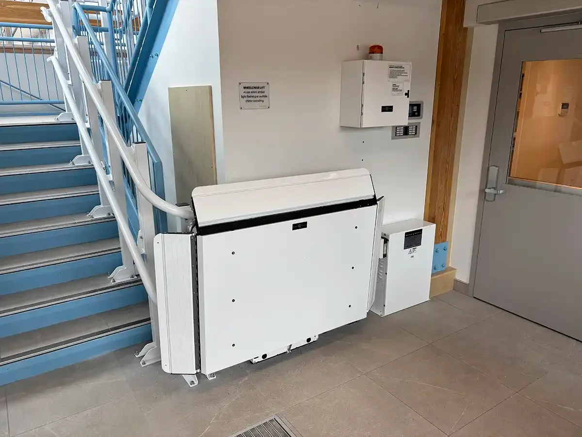 Folded inclined platform lift parked beside a commercial staircase with metal railings