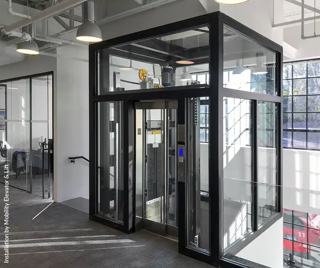 Glass-enclosed commercial elevator with black metal framing in a modern office interior