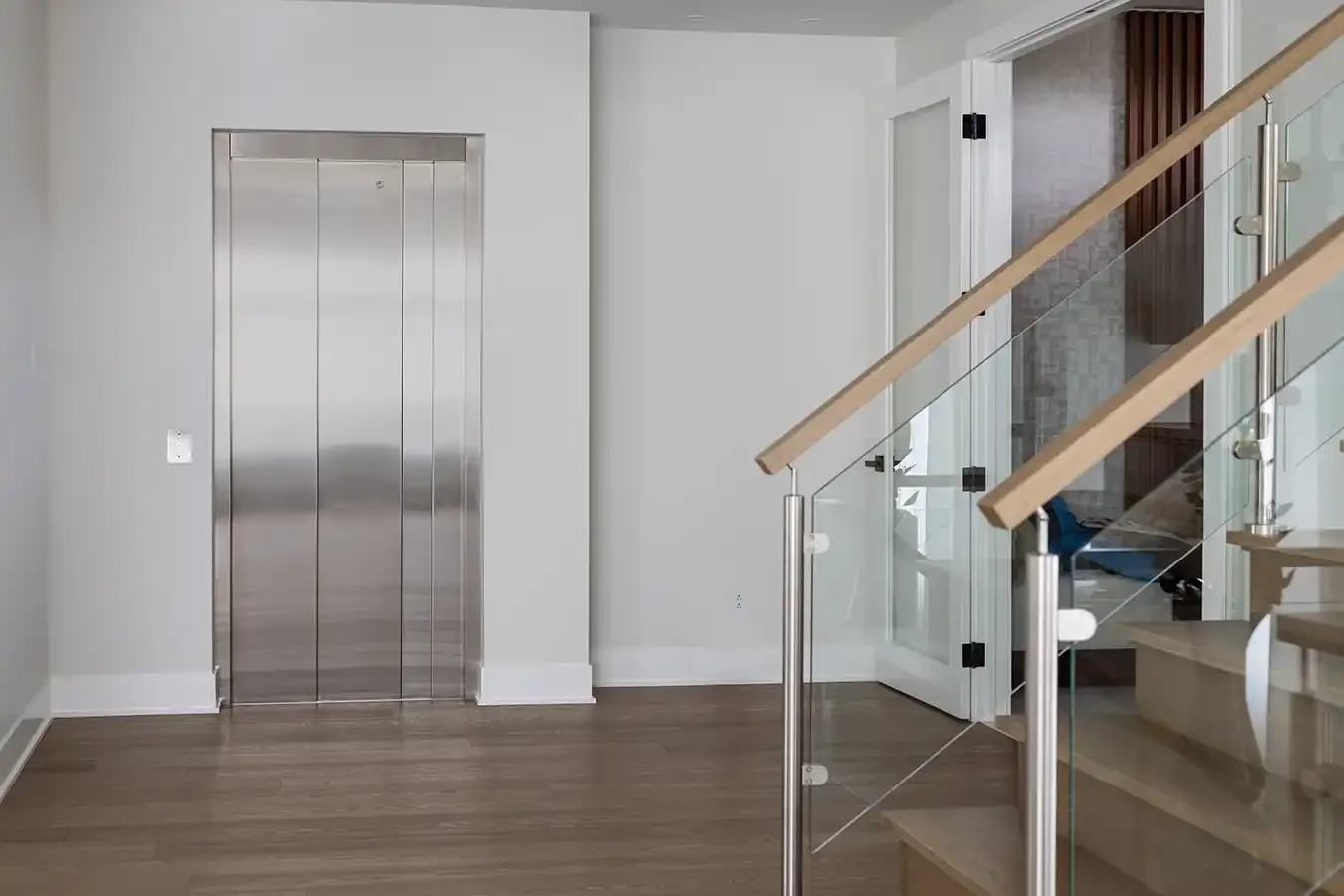 Modern home interior with a stainless steel residential elevator beside a glass-railed staircase