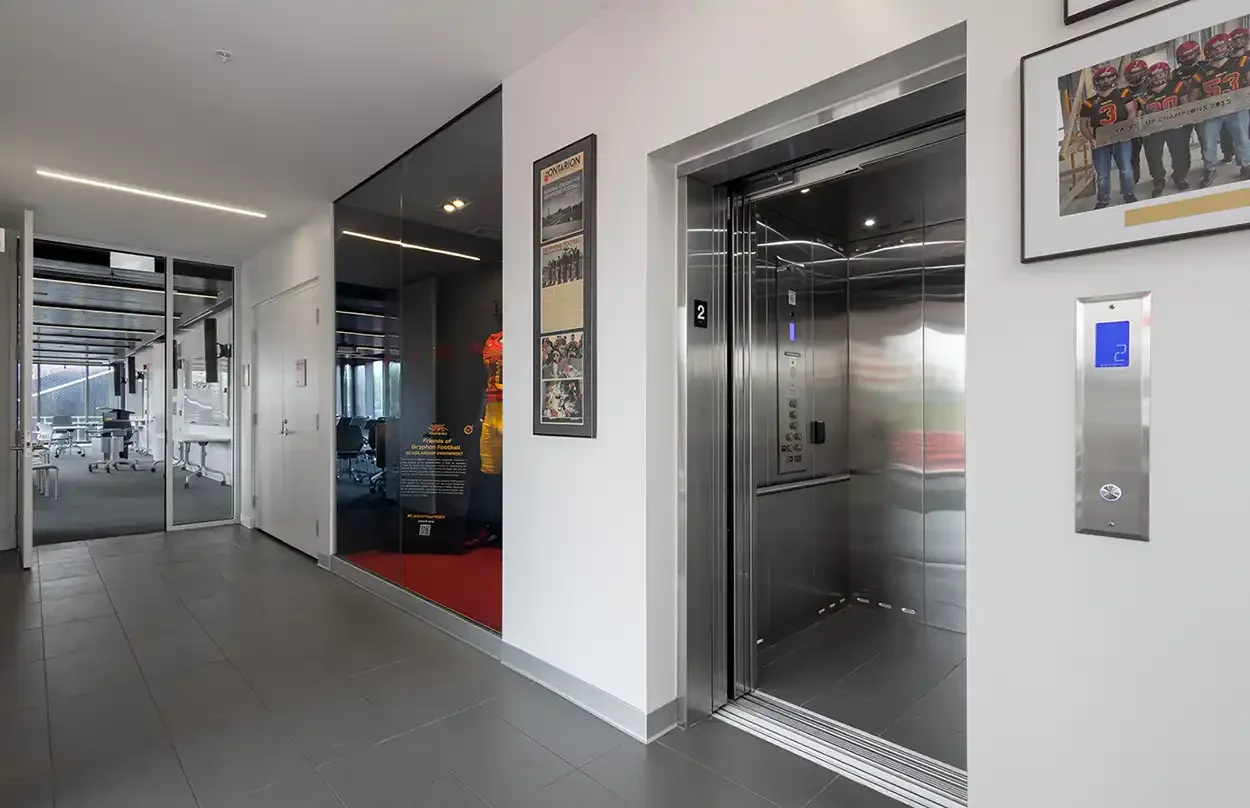 Modern office hallway with open stainless steel elevator and framed wall artwork