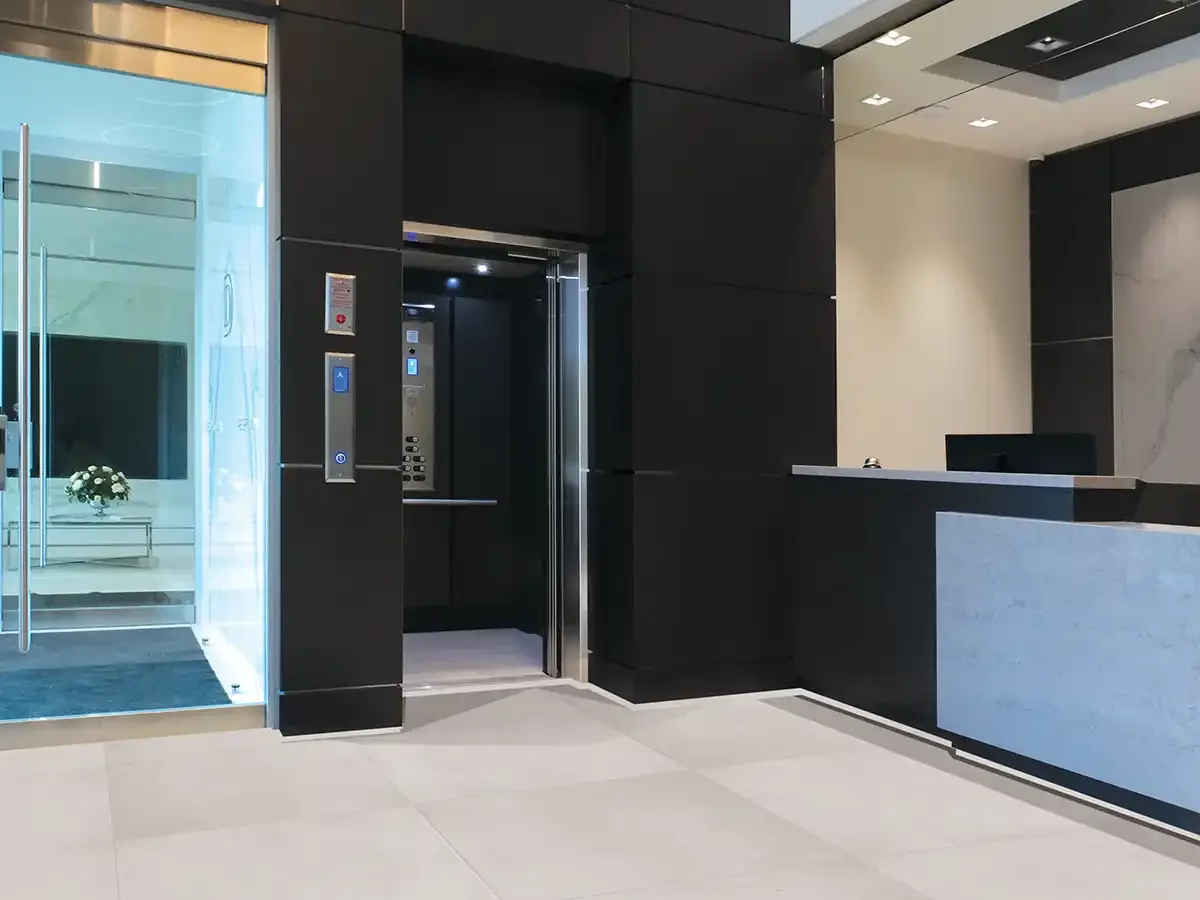Modern commercial lobby with black wall panels, open elevator, and reception desk