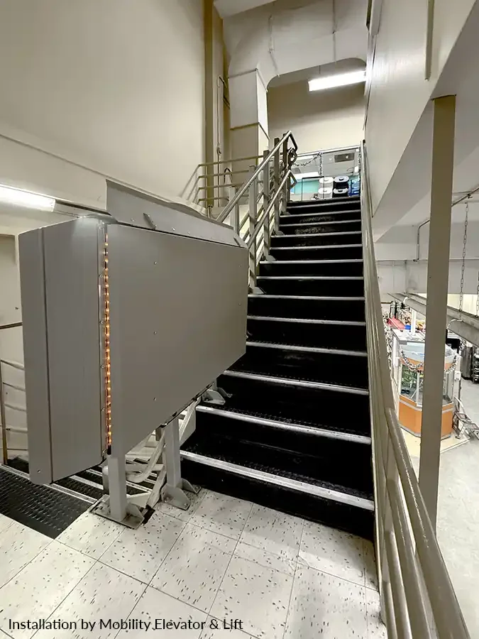Inclined platform lift installed alongside a commercial staircase with safety rails and control panel