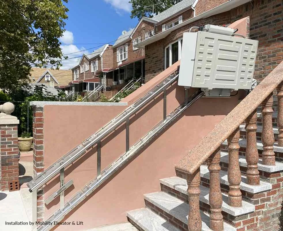 Savaria Delta inclined platform lift installed outdoors on a residential staircase, showing weather‑protected drive unit and rail system providing wheelchair accessibility between elevated entry levels.