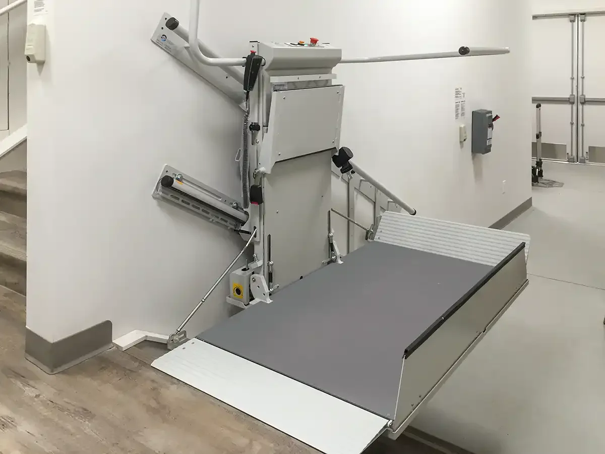 Savaria Delta straight inclined platform lift (IPL) with extended non-skid platform, side safety flaps, constant pressure controls, battery charging station, and manual lowering device at upper landing