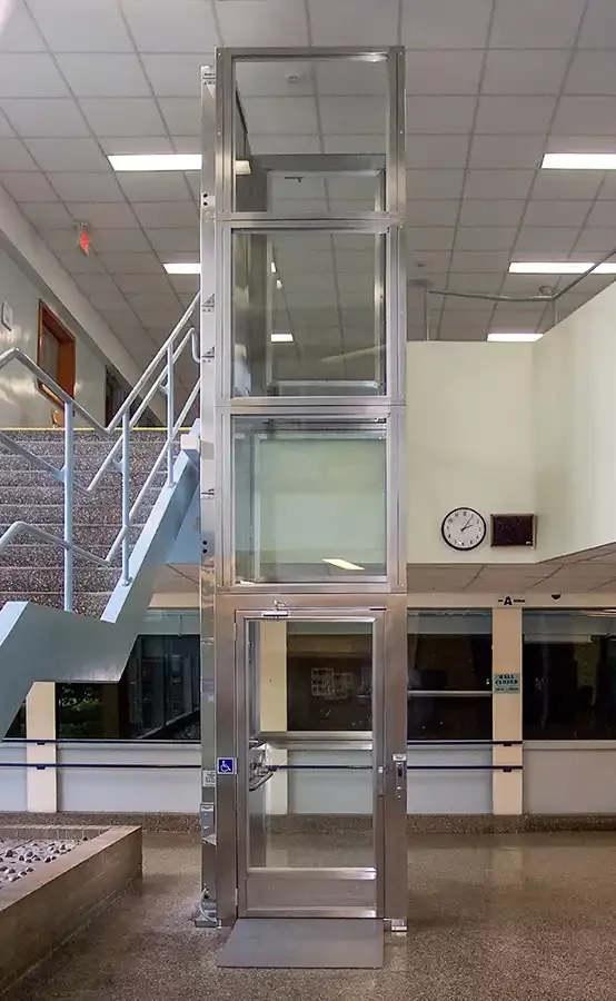 Glass-enclosed commercial platform lift spanning multiple floors inside a bright indoor atrium with stairs and railings