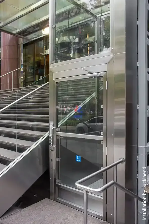 Glass-enclosed wheelchair platform lift integrated beside an exterior staircase at a commercial building entrance