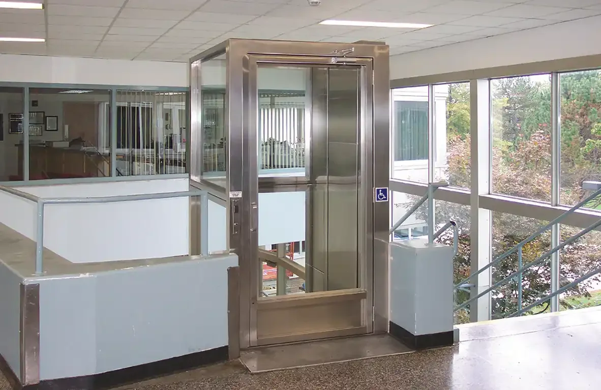 Glass-enclosed commercial elevator in an indoor atrium with railings and large windows overlooking trees
