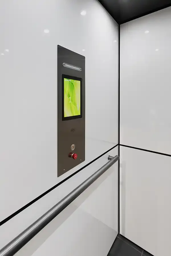 Residential elevator interior with white panels, digital control screen, and stainless steel handrail