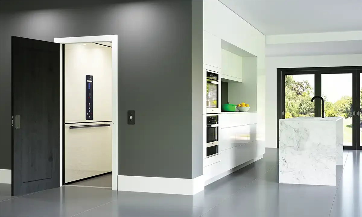 Open residential elevator integrated into a modern kitchen with marble island and dark cabinetry