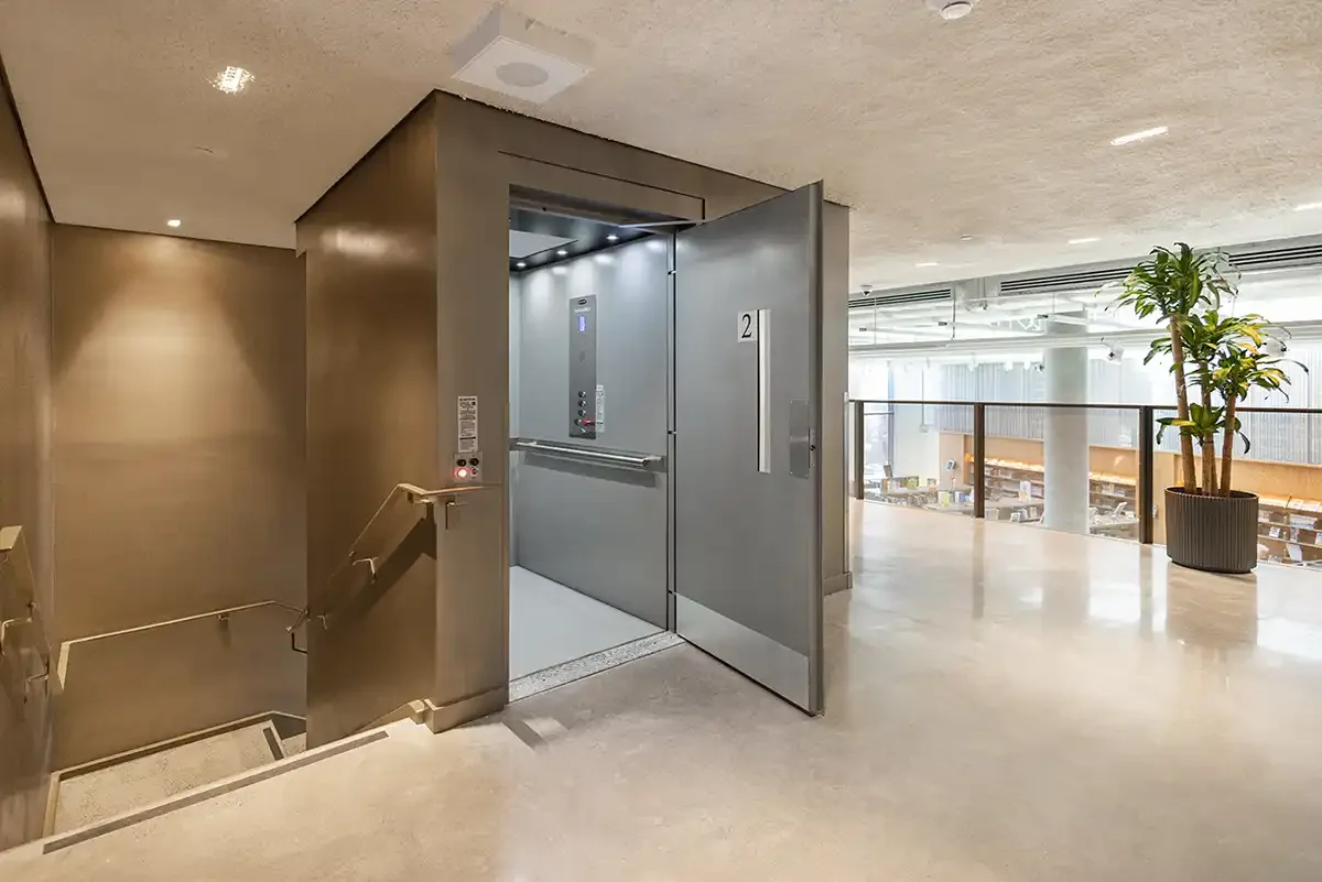 Open vertical platform lift behind a fire-rated commercial door in a modern public interior with open atrium views