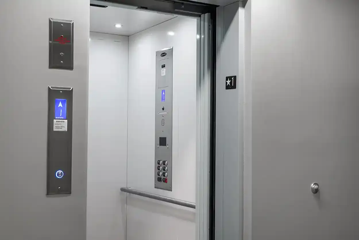 Modern commercial elevator interior with open door, illuminated control panel, call buttons, and handrail, providing accessible vertical transportation within a commercial or residential building.