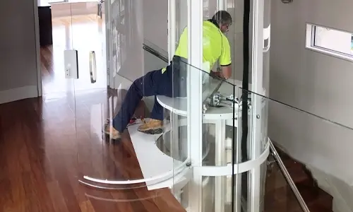 An elevator technician in process of installing a white framed Savaria Vuelift Mini winding drum elevator.
