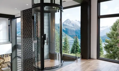A round glass elevator in a modern home overseeing mountains and trees in the background.