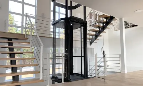Multi level staircase with an octagonal acrylic winding drum elevator in the middle.