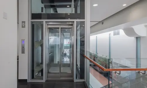 Glass door elevator with silver frame on the upper level of a commercial complex.