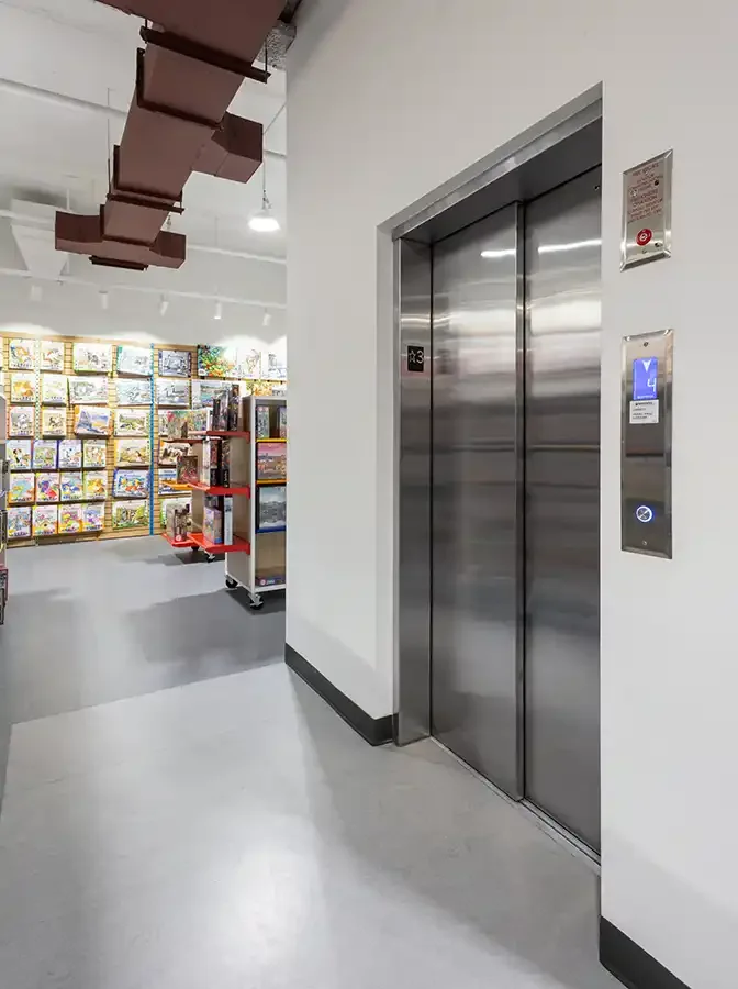 Savaria Orion LU/LA commercial elevator with brushed stainless steel automatic sliding doors, digital hall call station, and ADA-compliant signage in retail store hallway