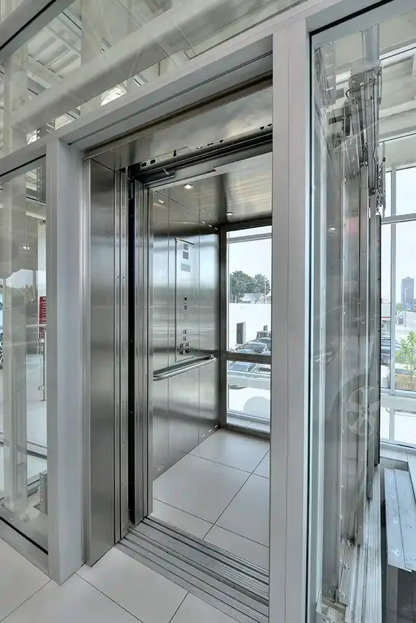 Savaria Orion LU/LA elevator with glass cab walls, stainless steel frame, automatic sliding doors, and handrail in modern retail building with natural lighting