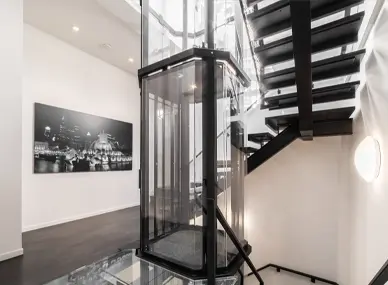 Panoramic glass residential elevator with square cabin design installed beside a modern staircase in a contemporary luxury home.