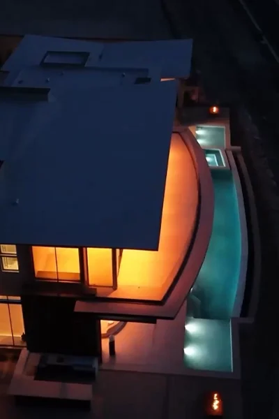 Nighttime aerial view of a modern home with glowing interior lights and a curved outdoor pool, overlaid with text about views of the desert and the Vegas Strip.