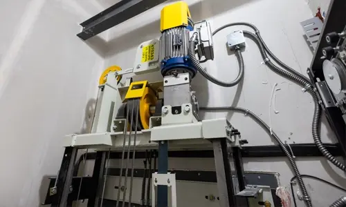 Close-up of elevator hoisting mechanism with electric motor, cables, and control components.