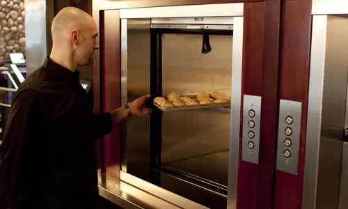 A chef loads a tray of baked goods into a material lift to move them to another level of the restaurant.