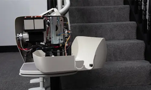 Curved Stair lift with its side cover removed, showing exposed motor and wiring on a carpeted staircase.