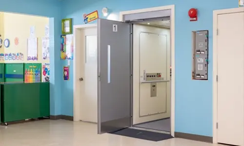 A vertical platform lift installed in a primary school with sky blue painted walls.