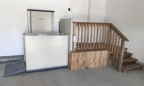 Residential porch lift positioned next to a short set of wooden steps inside a garage.