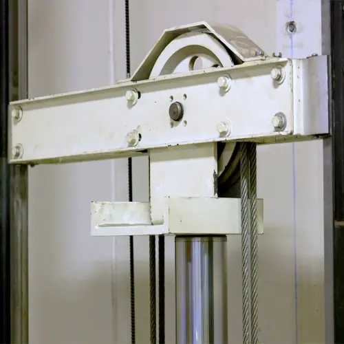 Hydraulic elevator system component showing a hydraulic piston with attached sheave assembly, where steel cables run over the sheave to lift and lower the platform as the piston extends and retracts.