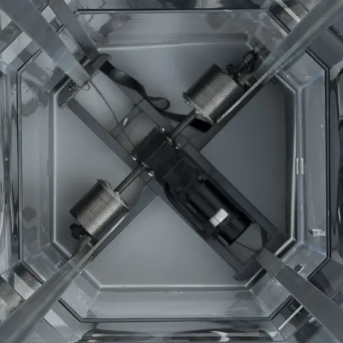 Winding drum drive system shown from an overhead view, featuring two steel cable drums mounted on opposite sides of a central motor, with the cables spooled around each drum and guided vertically within the surrounding frame structure.