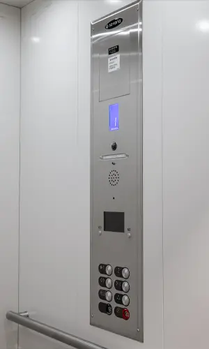 Stainless steel elevator control panel with illuminated floor indicator, emergency call speaker, and push buttons mounted inside a modern residential elevator cabin.