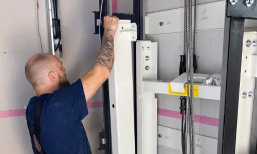 Technician performing maintenance on a residential elevator system inside a shaft, inspecting lift components and safety mechanisms.