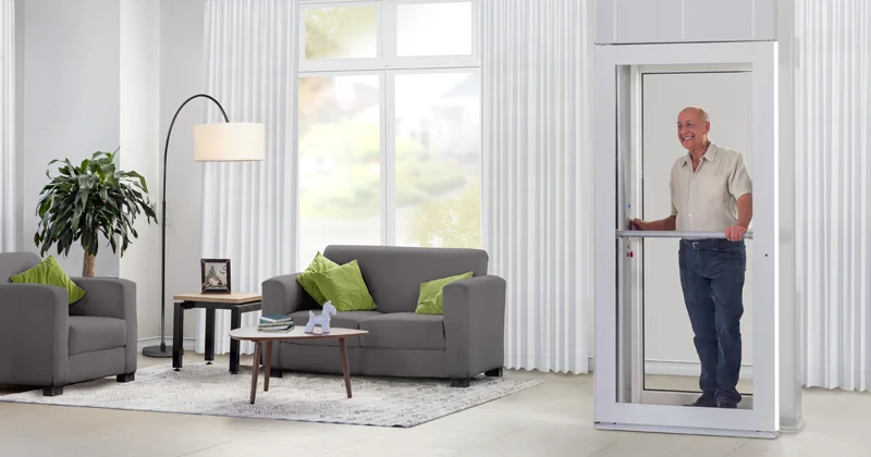 Luma through-the-floor home lift with glass cabin, featuring an older man using the residential elevator in a bright modern living room.